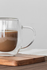 Close up of a bubble glass cup of coffe with milk on a wooden board on a tablecloth. Copy sapace.