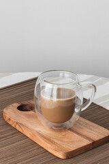 Bubble glass cup of coffe with milk on a wooden board on a tablecloth. Copy sapace in grey backgruond.