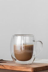 Bubble glass cup of coffe with milk on a wooden board on a tablecloth. Copy sapace in grey backgruond.