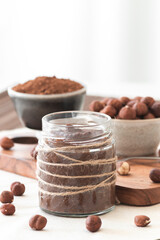 Homemade cocoa cream with hazelnuts in a jar on a tableboard. Sweet and healthy food. Front view with copy sapce. Focus point.