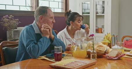 Happy couple having breakfast with teenage daughter sitting at kitchen table. The father is talking and the mother is serving juice to the daughter