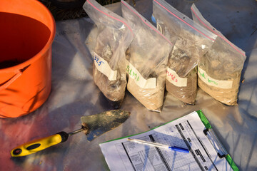 High angle view of sample bags with soil samples, garden tool, information sheet form outdoors. No...