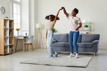 Mother and daughter leisure. Young african american woman with her dark skinned teenage daughter are dancing while enjoying weekend at home. Family, generation and people concept.