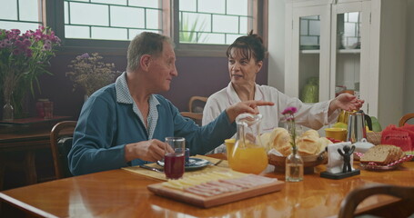 Fototapeta na wymiar Married couple having breakfast together. The wife serves coffee to her husband. the two chat happily and enjoy a good cup of coffee wearing pajamas