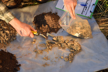 Closeup of agronomy specialist preparing soil samples for laboratory analysis outdoors. Professional farmer filling sample bag with material sampling at field. Environment research, soil certification