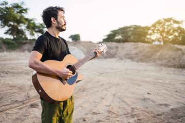 Portrait of young musician playing guitar on the road at sunset.
