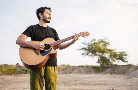 Portrait of young musician playing guitar on the road at sunset.
