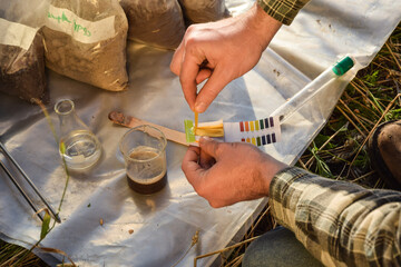 Closeup of agronomy specialist testing soil sample ph value outdoors, using laboratory equipment,...