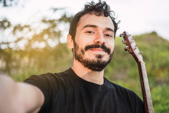 Young smiling Latin guitarist takes a selfie with his cell phone