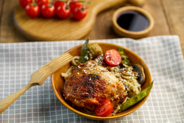 Udon with vegetables and chicken on the table in a wooden plate next to champignons and tomatoes and soy sauce on a plank.