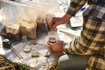 Male agronomy specialist testing soil sample outdoors, using laboratory equipment, performing soil...