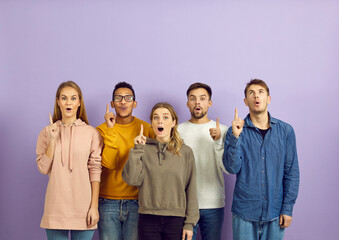 Young diverse mixed race people who found solution or were struck by bright idea standing on purple color background and pointing index fingers up with open mouths and happy surprised face expressions