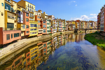 Fototapeta na wymiar Houses of colorful colors on the banks of the river and reflection in the calm water on a sunny day, Girona, Catalonia.