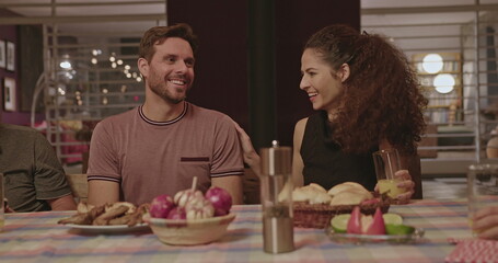 Family and friends in the evening together around the table in the backyard talking and laughing. Group of people celebrating holidays together around dinner table