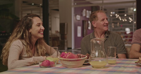Family and friends in the evening together around the table in the backyard talking and laughing. Group of people celebrating holidays together around dinner table