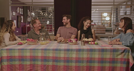 Happy family members talking in the evening while sitting at the table outside in the backyard home...