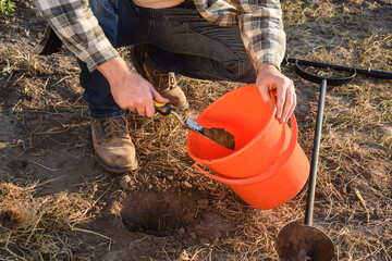 Male agronomist taking sample with soil probe sampler at agricultural field at sunrise. Farmer...
