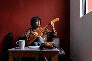 A young Mexican musician is composing a song with his jarana guitar at home