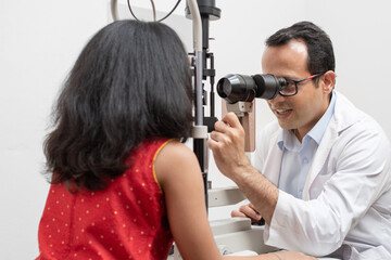 Naklejka premium Indian optometrist doing eye test with slit lamp in modern ophthalmology clinic, checking retina of a girl eye