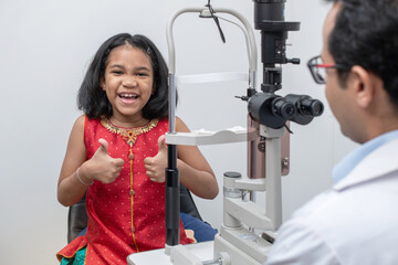 slit lamp, specialist, Indian girl in traditional costume thumbs up behind slit lamp in modern...