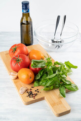 On a cutting board, ripe, red and yellow tomatoes, basil, a plate and olive oil in the background.
