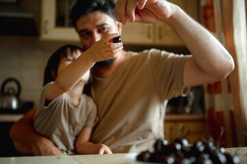 Dad and son sit in the kitchen at home and eat cherries. The concept of a happy family. Shallow depth of field