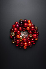 christmas portrait of a curious cat sticking head through red glossy christmas bauble wreath on black background with copy space