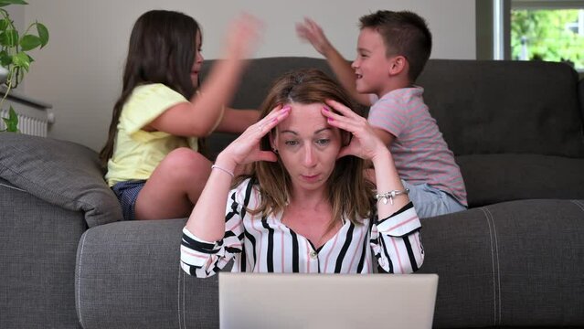 Tired busy woman working on laptop at home with her children. Single mother telecommuting stress. High quality 4k footage