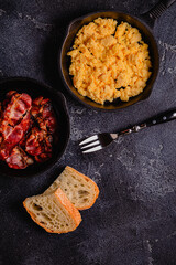 Cooked scrambled eggs and fried bacon in portion pans