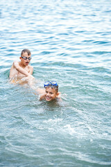 Siblings play together swimming in turquoise sea water near beach. Couple of brothers enjoys spending summer holidays at seaside playing in water