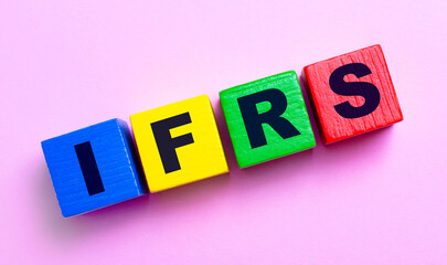 On a light pink background, multi-colored wooden cubes with the text IFRS International Financial Reporting Standards