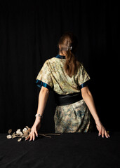 an elegant woman in a Chinese dress stands with her back to the camera on a black background and holds a bouquet of dried flowers in her hand