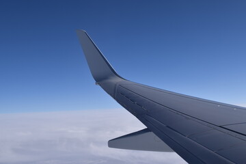 Window view of an airplane in the sky over clouds. Blue sky in the background. Traveling concept