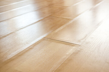 Swollen laminate flooring from flood or water damage, perspective view. Close up of light beige buckling laminate boards with bent edge pieces. Floor damage texture. Selective focus in center.