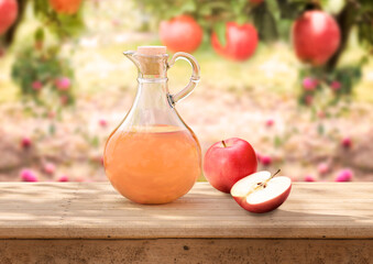 organic apple cider vinegar in glass jug on rustic wooden table apple orchard in background