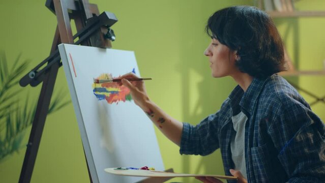A beautiful woman artists with short hair is using her amazing art skills to paint something beautiful on the canvas in an art studio. 4k
