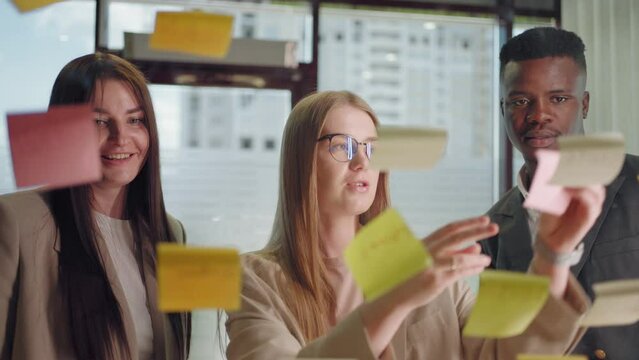 creative marketing specialists are brainstorming in office, sticking post-it notes on glass wall