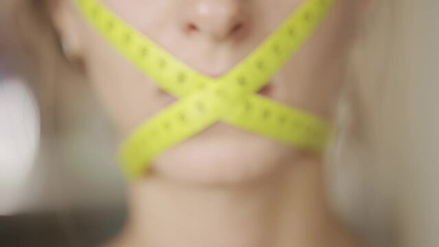 A woman with mouth tied in measuring tape is holding burger and dieting or having hard time with fast food. Big calories. Concept of unhealthy nutrition or weight loss and diet or fitness.