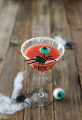 Terrifying red cocktail with spider on wooden background for Halloween with decoration. Vertical photo.