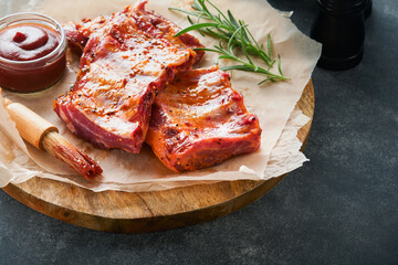 Pork ribs. Raw meat. Raw pork ribs in marinade with spices, rosemary, tomato sauce and garlic on old wooden stand on black stone table background. Barbecue concept. Selective focus. Mock up.