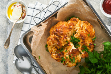 Baked cauliflower. Oven or whole baked cauliflower spices and herbs server on wooden rustic board on old grey background table. Delicious cauliflower. Eyal Shani dish. Perfect tasty snack.