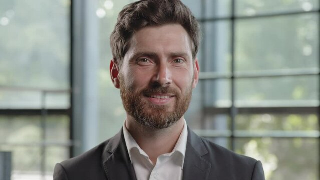Adult calm strong confident Caucasian 40s bearded man looking at camera with serious expression smiling dental toothy company CEO leader manager worker businessman posing indoors in office with smile