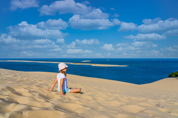 Girl sitting on a huge sand dune, famous tourist destination Dune Pyla. Pilat Dune in France.