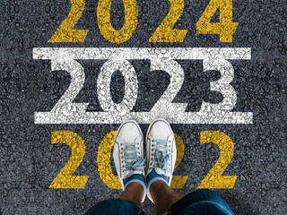 happy new year 2023. man legs in sneakers standing on asphalt road and number 2022 next to number...