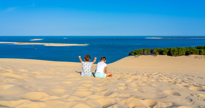 Girl and boy sitting on a huge sand dune, famous tourist destination Dune Pyla. Pilat Dune in France. High quality photo