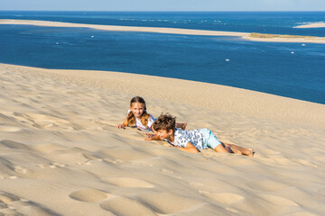 Girl and boy are playing on a huge sand dune, famous tourist destination Dune Pyla. Pilat Dune in France. High quality photo © Elena