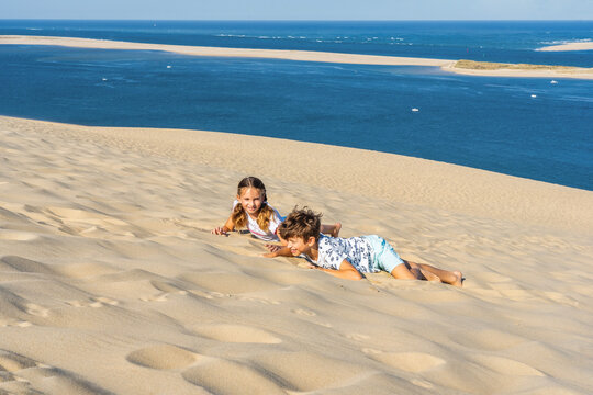 Girl and boy are playing on a huge sand dune, famous tourist destination Dune Pyla. Pilat Dune in France. High quality photo