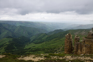 Fototapeta na wymiar Panoramic view of the canyon with green hills blurred by misty haze to the horizon and steep high cliffs of the Bermamyt plateau in Karachay-Cherkessia