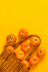 Fresh orange heirloom tomatoes in yellow crochet bag on a yellow background. Eco friendly shopping and zero waste concept. Top view. Copy space.