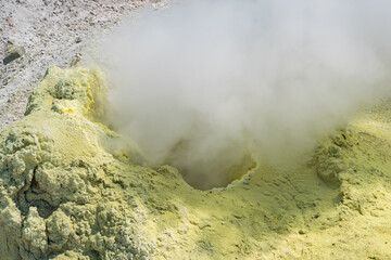smoking solfatara among sulfur deposits on a fumarole field on the slope of a volcano